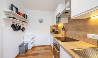 A modern kitchen with a wooden worktop and white furniture. Pots and kitchen utensils hang on the wall.