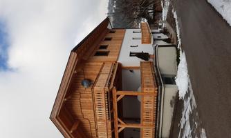 A charming wooden house with a large balcony and a snow-covered surroundings. The facade is white with wooden elements, surrounded by a tranquil landscape.