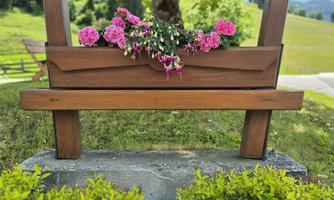 A wooden sign with the inscription "Schwarzkogler Hof" is adorned with colorful flowers. In the background, green meadows and a blue sky can be seen.