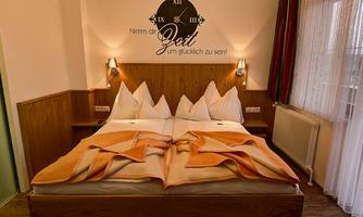 A cozy bedroom with a large double bed and elegant bedding. On the wall hangs a clock with the saying "Take time to be happy!"