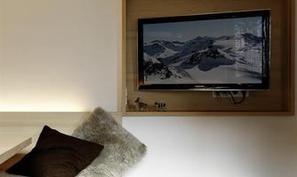 A modernly designed living space with a television on the wall. The furnishings consist of a wooden shelf, a cozy seating area, and a rug.