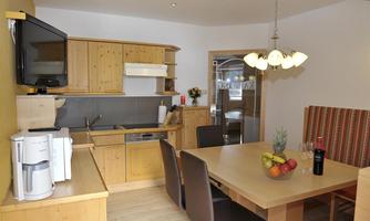 A modern kitchen with wooden furniture and a dining table. There is a refrigerator, a stove, and a cozy atmosphere.