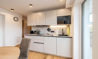 A modern kitchen with bright cabinets and a countertop. The room has wooden flooring and large windows that let in plenty of light.