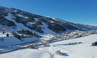 A picturesque winter landscape with snow-covered hills and a small village in the valley. The clear sky creates a calm and peaceful atmosphere.
