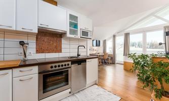 A modern kitchen with white cabinets and a wooden workspace. Large windows let in a lot of light and offer a view of the outdoors.