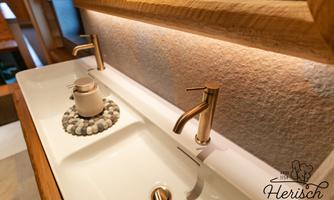 A modern bathroom with an elegant double sink and golden faucets. The lighting and stone decoration create a cozy atmosphere.
