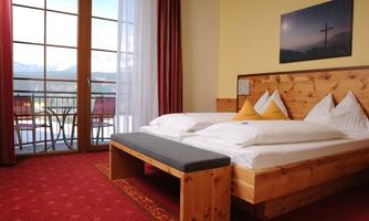 A cozy room with a large bed and wooden furniture. The balcony offers a beautiful view of the mountains.