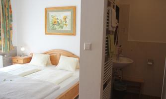 A cozy bedroom with a double bed and a colorful mural. Adjacent is a modern bathroom with a sink and toilet.