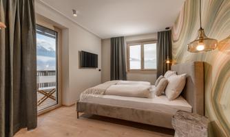 A modern bedroom with a large bed and elegant decor. Large windows provide plenty of light and a view of the mountains.