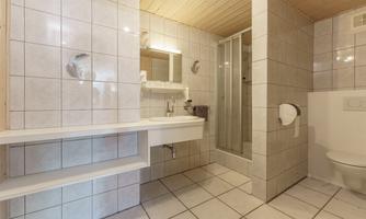 A modern bathroom with tiled walls and a bright wooden ceiling. There is a shower, a sink, and a toilet.