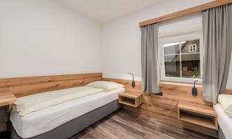 A bright room with two single beds and wooden details. The window offers a view of the exterior of the building.