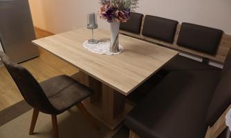 A modern dining area with a wooden table and a bench. A vase with flowers and a candle holder are on the table.