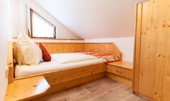 A cozy bedroom with wood paneling and a skylight. The room is furnished with a bed and a dresser.