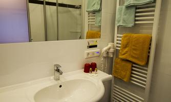 A modern bathroom with an oval sink and a towel warmer. Subtly decorated with towels and toiletries.
