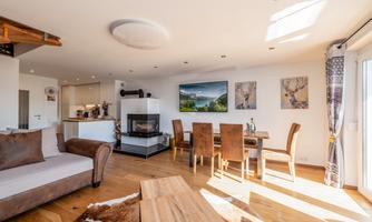 A modern living room with a cozy couch and a dining table. Large windows provide plenty of daylight and an inviting atmosphere.