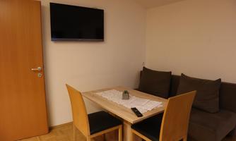 A cozy living area with a dining table, chairs, and a sofa. A television hangs on the wall.