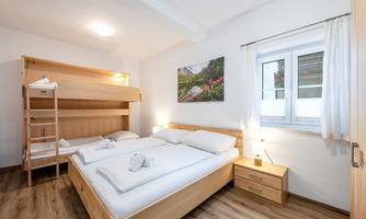 A bright room with a double bed and a bunk bed.  
On the wall hangs a picture of a blooming landscape.