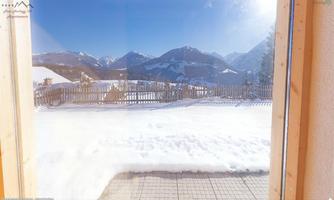 A picturesque winter landscape with snow-covered ground and high mountains in the background. The view is clear and exudes tranquility.