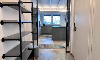 A modern hallway with an open space in the background. On the left side, there is a shelf and the walls are brightly designed.
