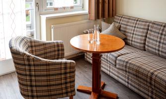 A cozy living area with a checkered armchair and a couch. A round table with glasses is in the center of the room.