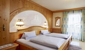 A cozy bedroom with wooden paneling. It contains two single beds, lamp-like nightstands, and a window with curtains.