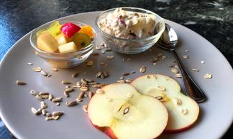 A plate with fresh fruit salad, a bowl of yogurt, and some apple slices. Next to it are oatmeal and a spoon.