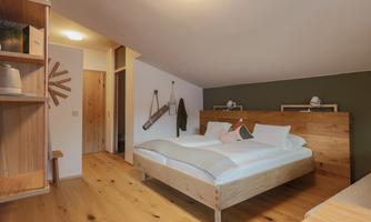 A modern bedroom with a large wooden bed and minimalist decor. The walls are painted in soft colors, and the floor is made of light wood.