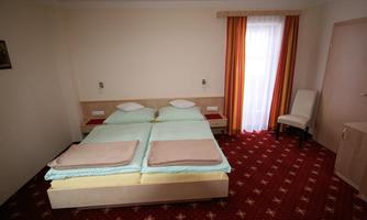 A simple bedroom with a double bed and two nightstands. The room has light-colored walls and curtains in warm tones.