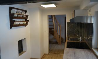 A modern kitchen with a wooden worktop and a rack for dishes. In the background, there is a staircase and a bright, open space.