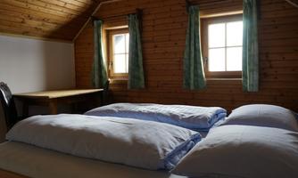 A cozy room with wooden paneling and two windows. There are two beds with white bedspreads and a small table.