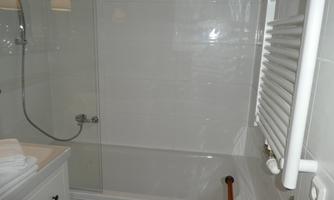 A modern bathroom with a bathtub and a shower. There are bright tiles and a towel radiator on the wall.