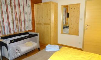 A cozy bedroom with a crib, a wardrobe, and a large mirror. The walls are bright and the windows have colorful curtains.