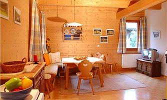 A bright and inviting kitchen with wooden walls and a dining area. There is fruit on the table and cozy seating options.