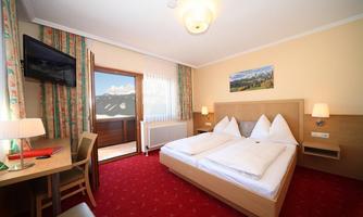 A cozy hotel room with two beds and a table. There is a beautiful view of the mountains through the window.