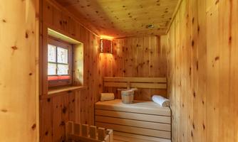 A cozy wellness area with wooden walls and a wooden bench. The sauna has a window and is softly lit.