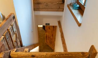 A cozy wooden staircase leads down. The room has a warm, inviting ambiance with a window and a picture frame.