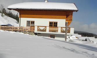 A house in the snow with a wooden balcony and a bright facade. The surroundings are covered by a sparkling snow blanket.