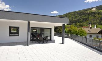 A modern terrace with a viewpoint of the mountains. The terrace has bright tiles and features a table with chairs.
