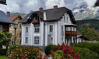 A beautiful, historic building with a blue facade and a balcony. Surrounded by colorful flowers and a picturesque landscape under a cloudy sky.