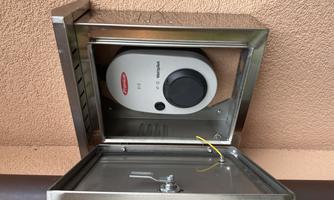 A modern wall socket for electrical connections is mounted in a metal cabinet. The cabinet is open and shows the control unit and the wiring.