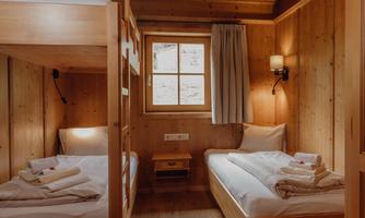 A cozy room with wood paneling and two beds. On one bed is a bunk bed, and the room has a window with a curtain.