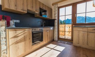 A modern kitchen with wooden cabinets and a window front that reveals the view of the mountains. The kitchen is bright and inviting.