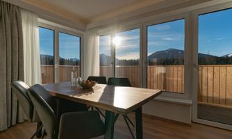 A modern dining room with a wooden table and elegant chairs. Large windows offer a view of the mountains and let in plenty of sunlight.