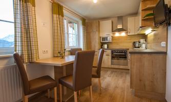 A modern kitchen with wooden cabinets and a dining area. There is a table with chairs as well as appliances like a stove and a microwave.
