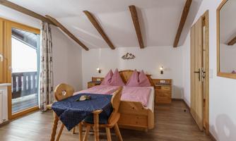 A cozy bedroom with two single beds and wooden decor. The room features a balcony and large windows that allow plenty of natural light in.