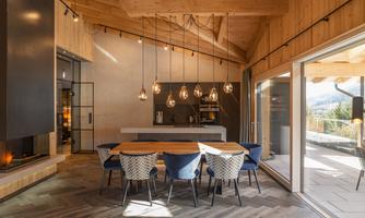 A modern dining room with a large wooden table and stylish chairs. The large windows allow plenty of light in and offer a view of the surrounding nature.