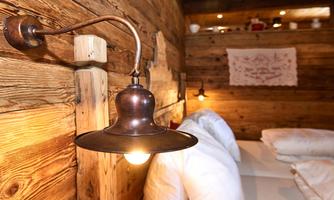 A cozy bedroom with wood paneling and soft lighting. On the bed are pillows and blankets that create an inviting atmosphere.