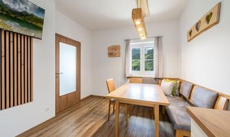 A bright dining room with a wooden tray and a bench.  
There is a window with a view of the mountains and decorative pictures on the walls.