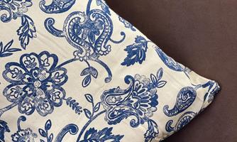 A decorated cushion with a blue floral pattern. It is placed on a brown sofa.