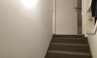 A staircase leads to a closed door. The hallway is brightly lit and designed in a minimalist style.
